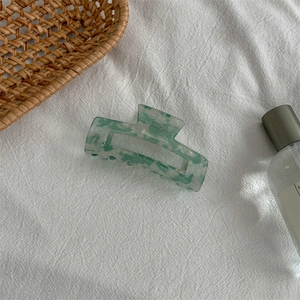 Detailed close-up of a square marbled acetate hair claw clip with green and white patterns