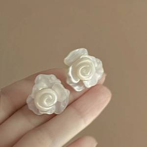 Nahaufnahme eleganter weißer 3D-Harzrosen-Ohrringe mit Perlmuttglanz in der Hand