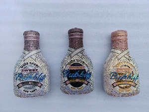 Three crystal-encrusted champagne bottle clutch bags in silver, gold, and black colors