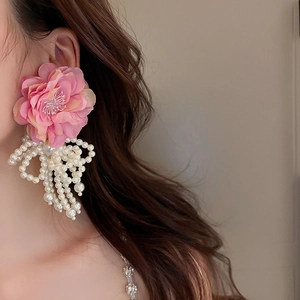 Close-up of pink fabric flower earrings with white pearl tassels worn by a model