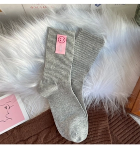 Détail de chaussettes grises en tricot avec écusson rose smiley et texte SMILE sur peluche