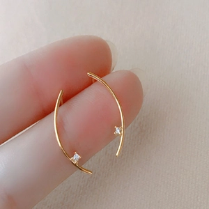 Gold curved stud earrings with white zircon accents held between fingers for size