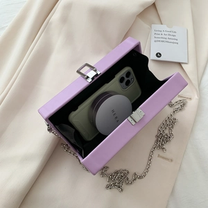 Purple textured small square bag with silver chain strap shown on cream fabric background