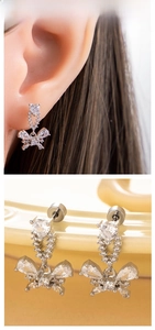 Macro detail of silver heart and zircon butterfly drop earrings on a ceramic dish