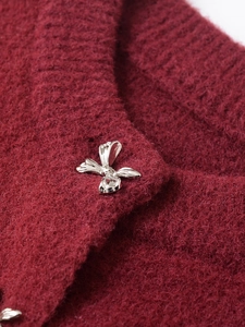 Macro detail of wine red mohair knitwear featuring a silver metal bow button and rib texture