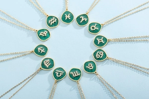 Flat lay of twelve gold zodiac necklaces with green malachite and crystal pendants