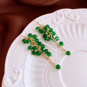 Macro detail of green beaded tassel earrings with gold chain on a vintage ceramic plate