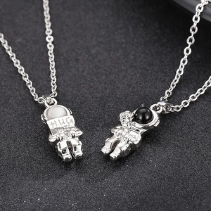 Astronaut pendant necklaces in silver finish featuring Hug Me engraving on a dark surface