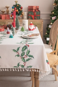 Detailed view of beige Christmas tablecloth with holly patterns and elegant white tassels