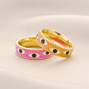 Golden evil eye rings with pink and orange enamel finish on satin background