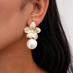 Close-up of golden flower earrings with white pearl drops worn by a female model