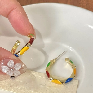 Detail of gold C-shaped hoop earrings with colorful enamel blocks and small crystals