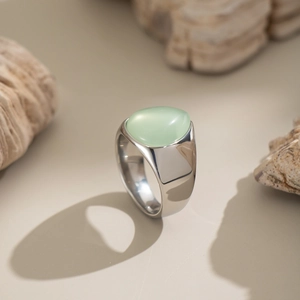 Détail d'une bague argentée avec pierre vert clair sur fond de sable naturel