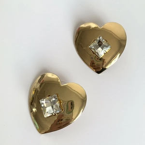 Detailed close-up of golden heart earrings featuring a square clear crystal center