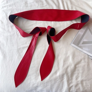 Ceinture large en cuir PU rouge et noir posée à plat sur un fond en tissu blanc plissé
