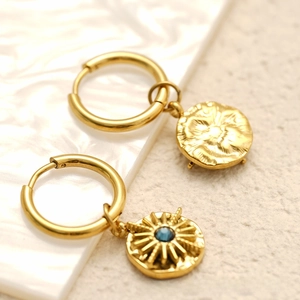 Detailed macro view of 18K gold hoop earrings featuring a blue zircon sunburst coin pendant