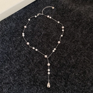 Détail d'un collier en Y avec des perles et un pendentif poli en forme de goutte d'eau