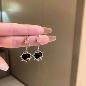 Close-up of thorn heart earrings in silver with black stone held by hand for size