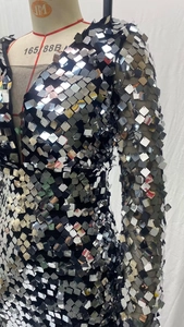 Gros plan de paillettes carrées argentées et de manches en maille noire sur une robe
