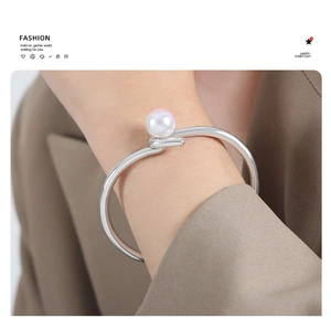 Detailed view of an open silver metal bracelet with a white pearl on a model's wrist