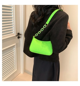 Detail of neon green crocodile pattern bag with chunky chain strap on a shoulder