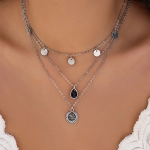 Detail of layered silver necklace featuring a black drop gem and vintage coin pendant
