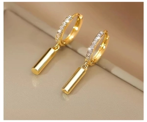 Macro shot of minimalist gold dangle earrings with small diamonds and a polished cylinder