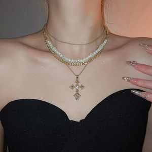 Detail of layered gold-plated necklace with faux pearls and a crystal cross pendant