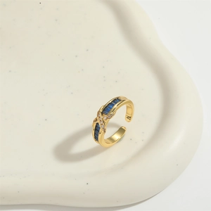 Minimalist adjustable golden X-shaped ring with blue rectangular stones and zircon accents