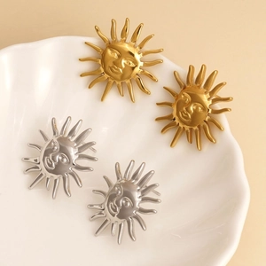Elegant gold and silver sun face earrings displayed on a white shell tray