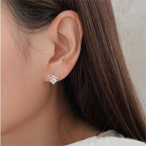 Macro side view of a minimalist silver bow earring with zircon stones on female model ear