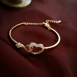Detail of gold heart bangle with pavé zircons and infinity charm on silk background