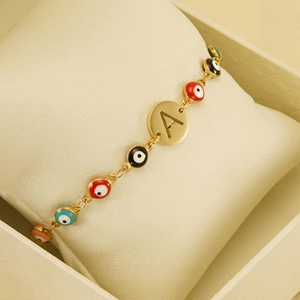 Golden Evil Eye bracelet with alphabet charm displayed on a jewelry pillow