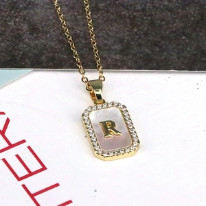 Detailed macro of 18K gold letter R pendant with shell inlay and zircon borders