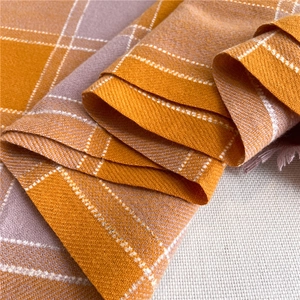 Close-up of soft plaid scarf fabric showing orange and grey weave with fringe details