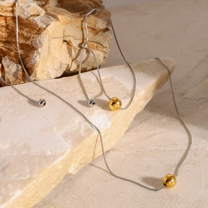 Minimalist snake chain necklace with gold sliding bead on natural stone pedestal