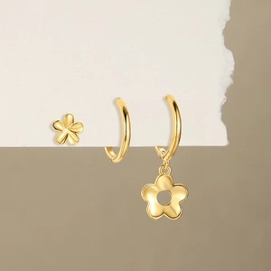 Détail de boucles d'oreilles fleurs dorées et anneaux sur papier blanc à bords déchirés