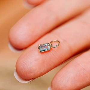 Macro shot of a rectangular gold pendant with a faceted light blue zircon on a finger