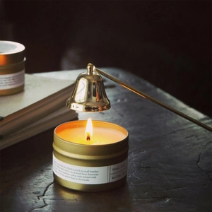 Golden bell candle snuffer extinguishing a burning soy candle in a warm vintage setting