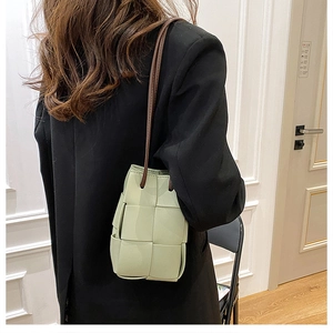 Close-up of a light green woven crossbody bucket bag with wide PU leather grid pattern