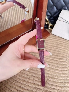 Close-up of small rectangular gold watch with red leather strap and diamond on dial
