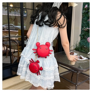 Street style view of a red crab-shaped crossbody bag and mini charm on a lace dress