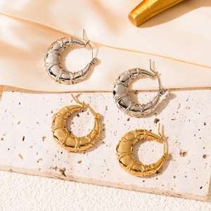 Detail of gold and silver C-shaped hoop earrings with bamboo texture on stone background