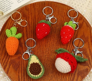 Macro view of handmade crochet fruit keychains including strawberry and avocado on wood