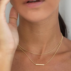 Double-layered gold stainless steel necklace with T-bar pendant worn by a model
