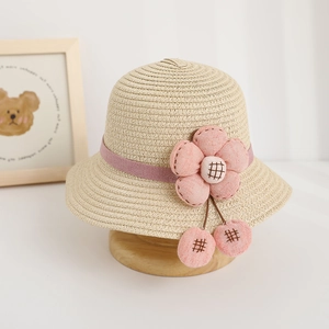 Detailed view of children straw hat with pink fabric flower and ribbon on wooden base