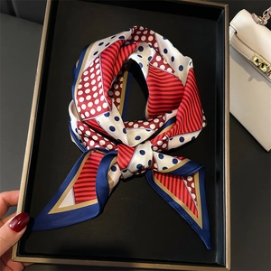 Polka dot and stripe silk scarf in red and navy draped over a black tray and handbag