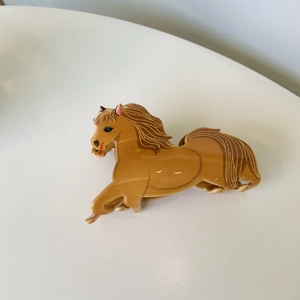 Detailed view of a glossy caramel brown pony-shaped hair claw clip on a white surface