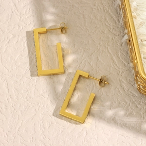 Close-up of gold plated rectangular earrings with crystal stones on a textured background