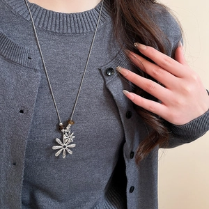 Long silver necklace with double floral pendants and tiger eye bead on a gray cardigan